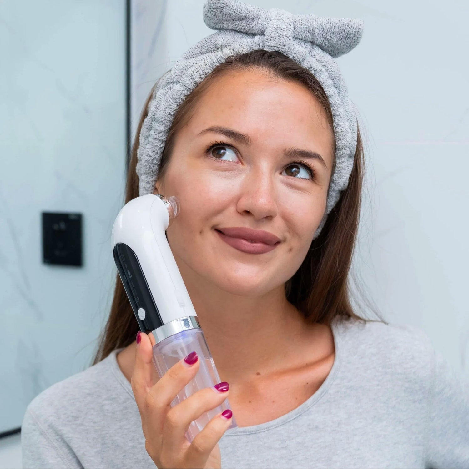 Jeune femme utilisant un appareil Hydrafacial pour nettoyer et hydrater la peau de son visage. Soin beauté moderne pour un teint frais et lumineux. Accessoire disponible chez MONDOBOX.

